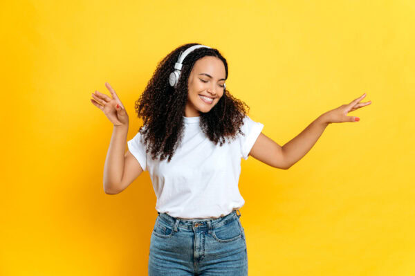 Listening to music with headphones, smiling, against a yellow background.