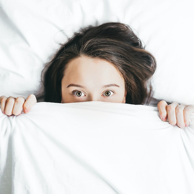 A lady in bed with the covers pulled up to her eyes but not sleeping