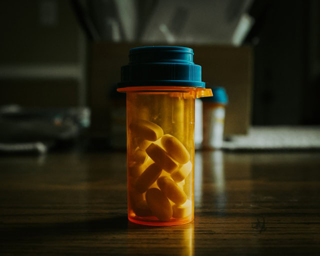 Prescription pill bottle with yellow pills inside, on a wooden surface.