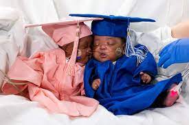 2 babies dressed in a cap and gown for graduation