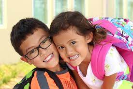Two kids in backpacks hugging one another